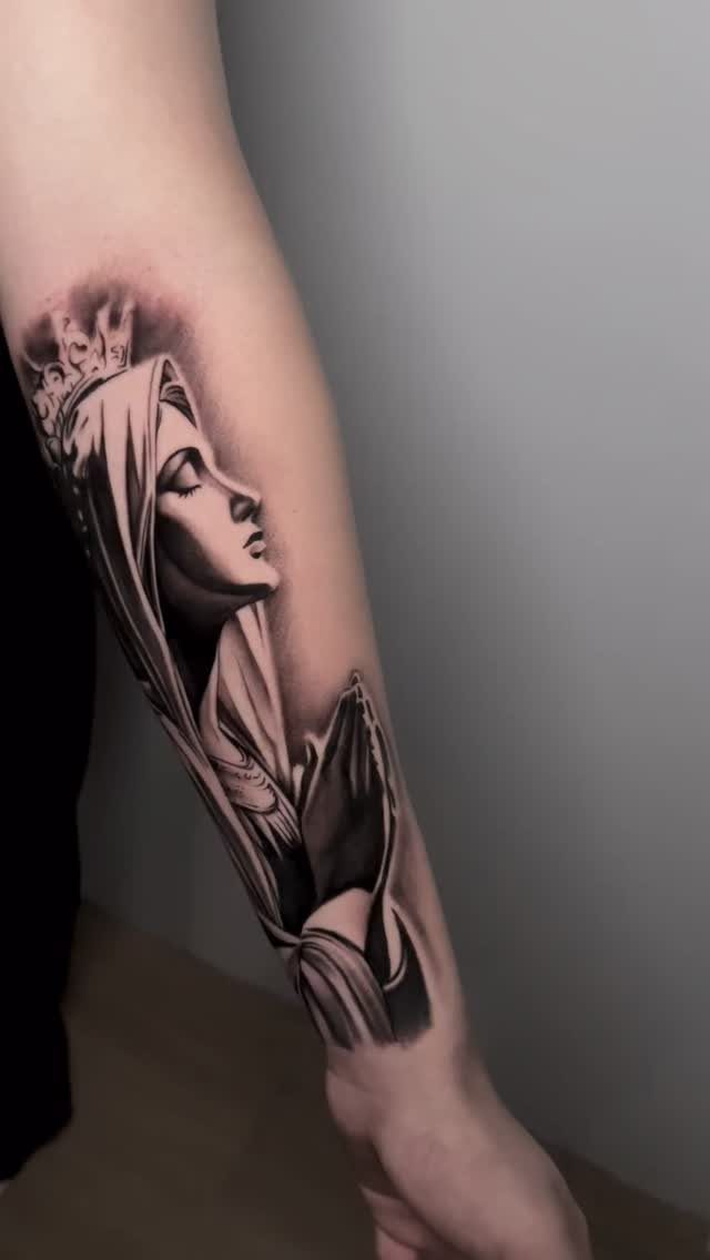 Virgin Mary tattoo on a forearm featuring detailed black and grey shading.