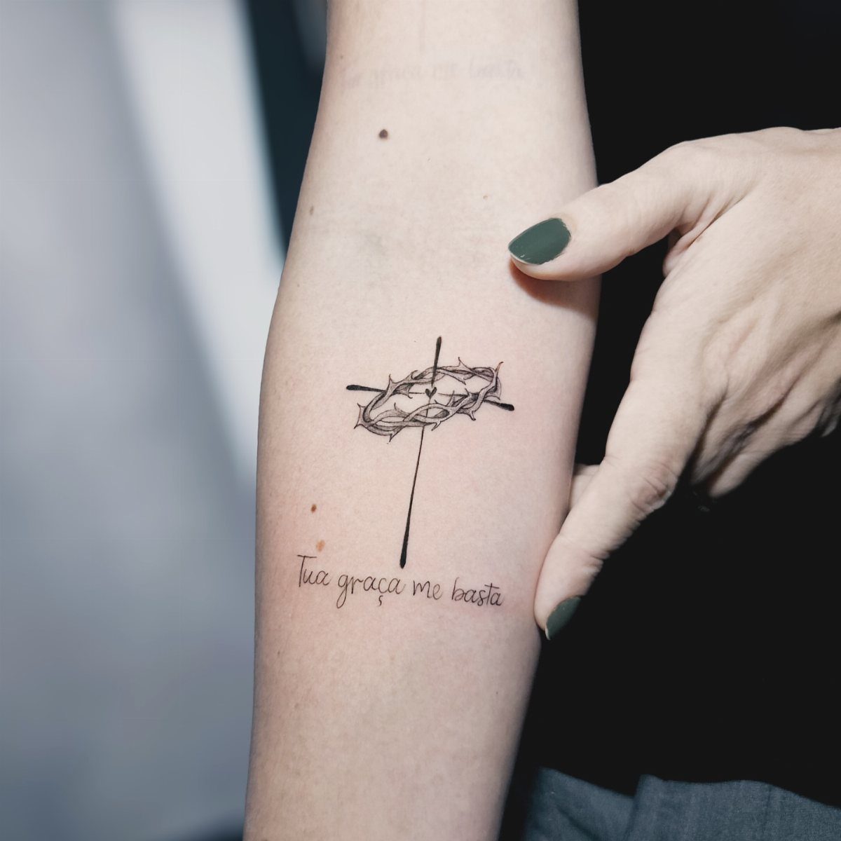 Forearm tattoo of a cross with a crown of thorns and Portuguese script.