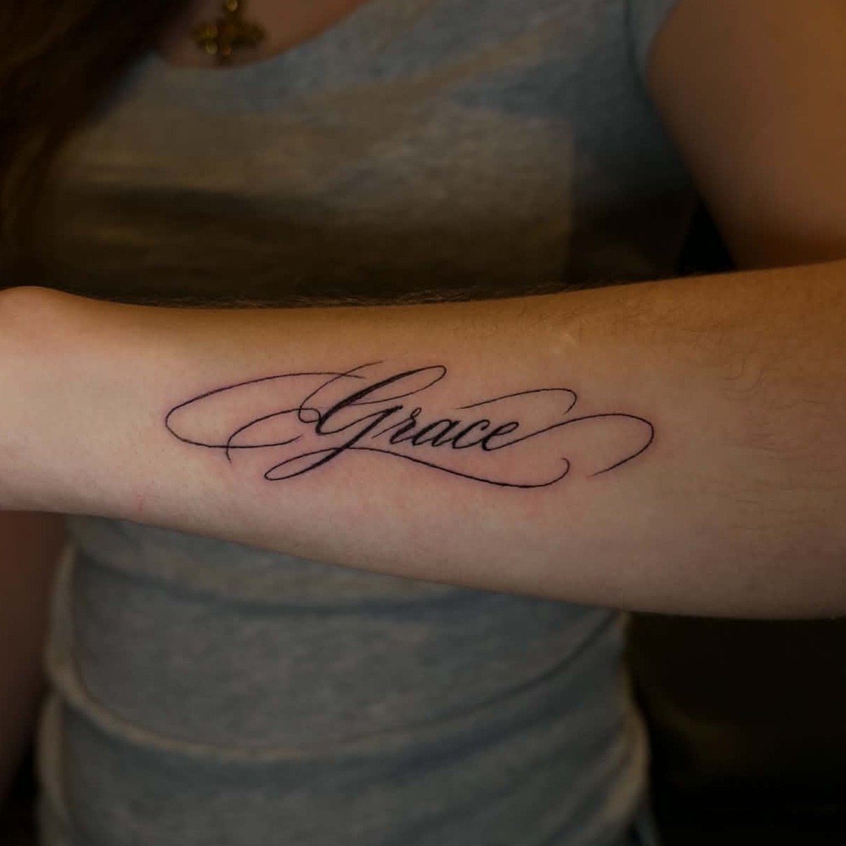 Forearm tattoo of the word Grace written in elegant black cursive script.