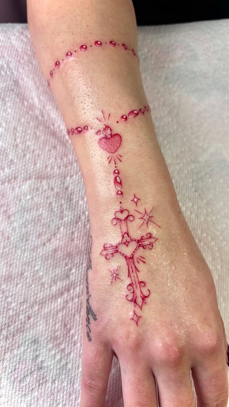 Red rosary tattoo on a wrist featuring a heart and decorative cross.
