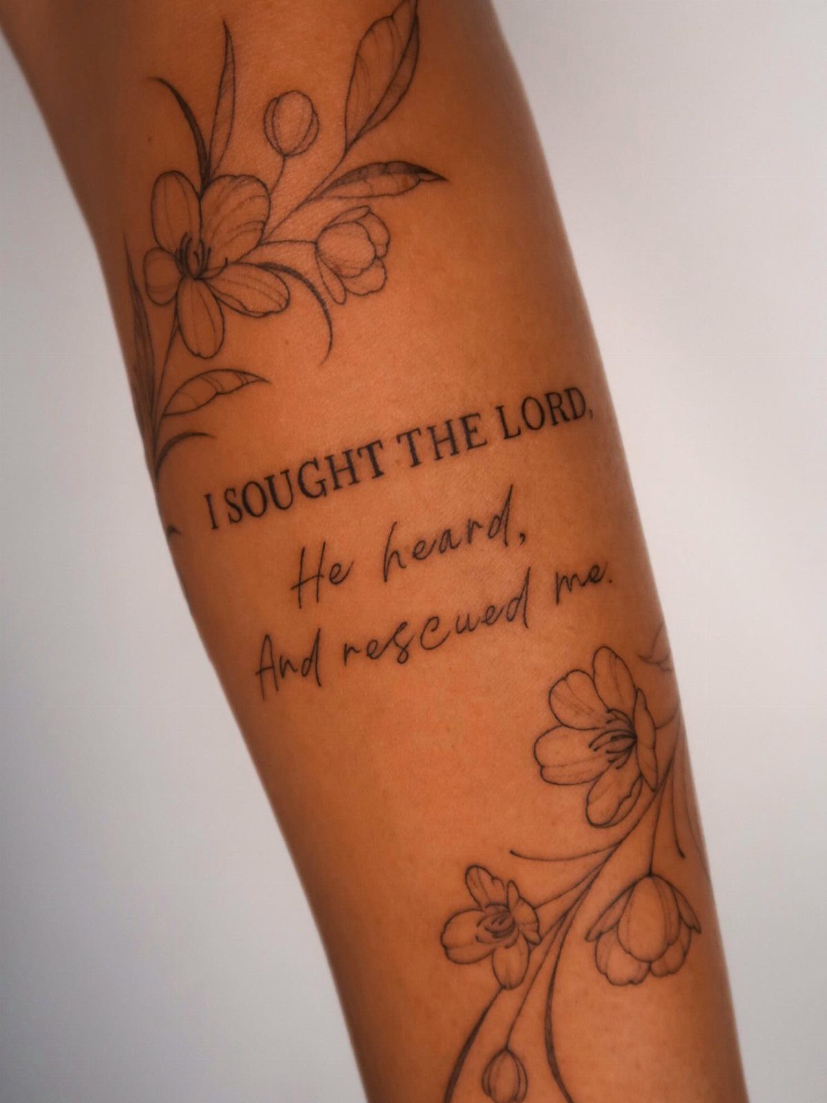 Forearm tattoo with floral designs and a religious quote about seeking the Lord.