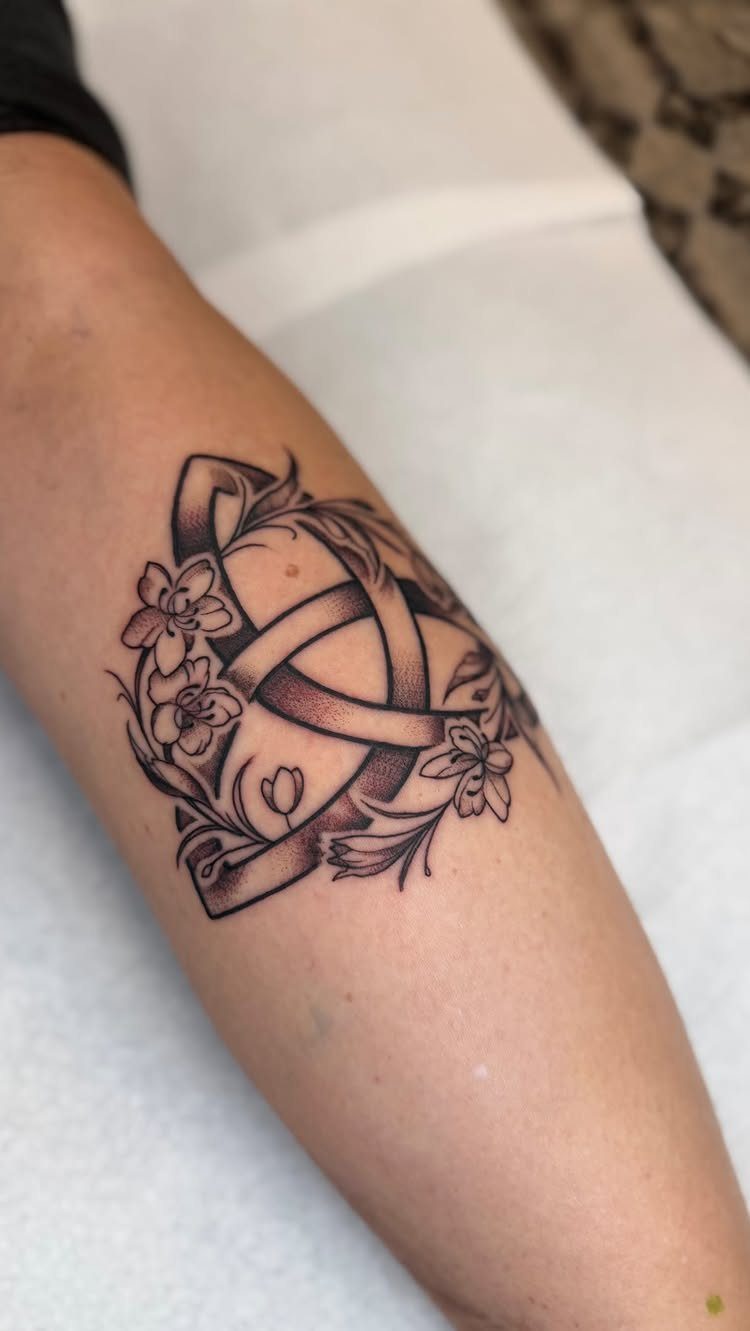 Trinity knot tattoo with floral elements on a person's forearm in black ink