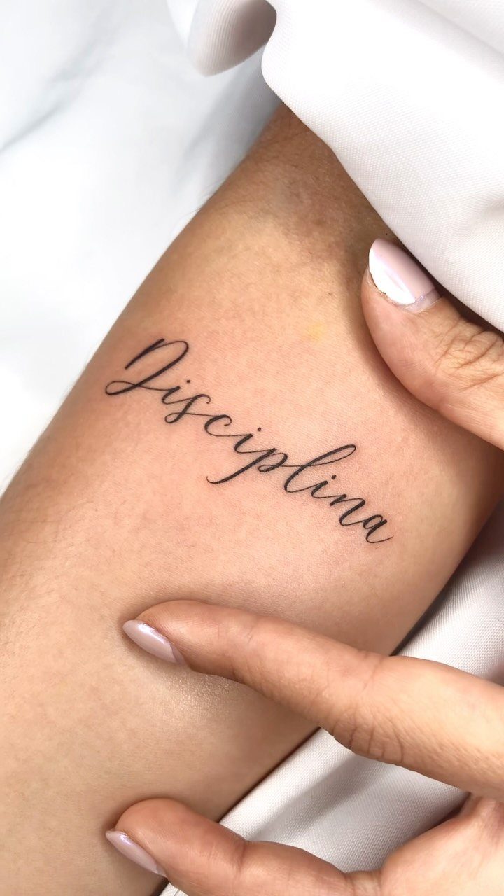 Cursive script tattoo of the word Disciplina on a person's forearm