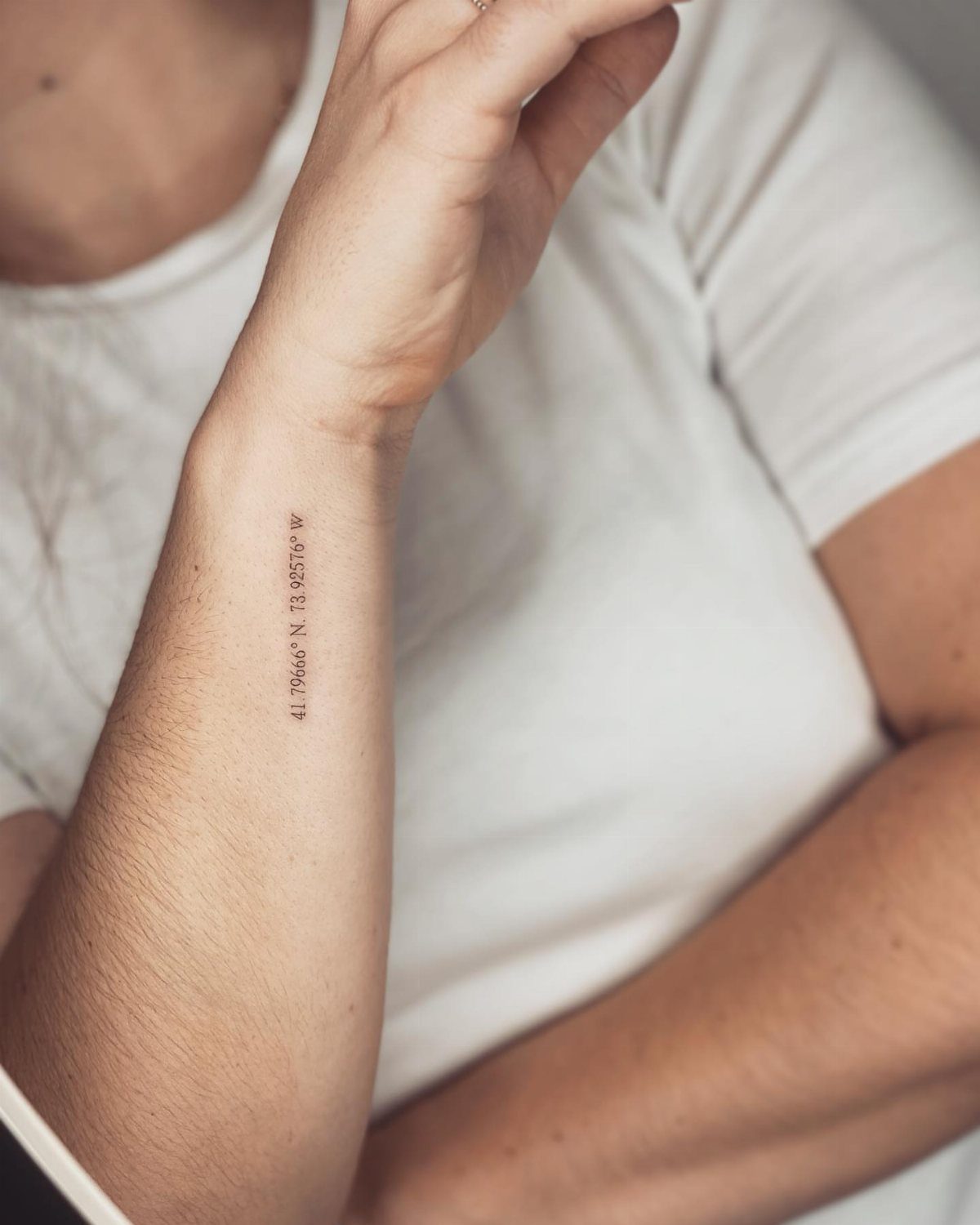 Small black ink tattoo of geographic coordinates on a person's inner wrist