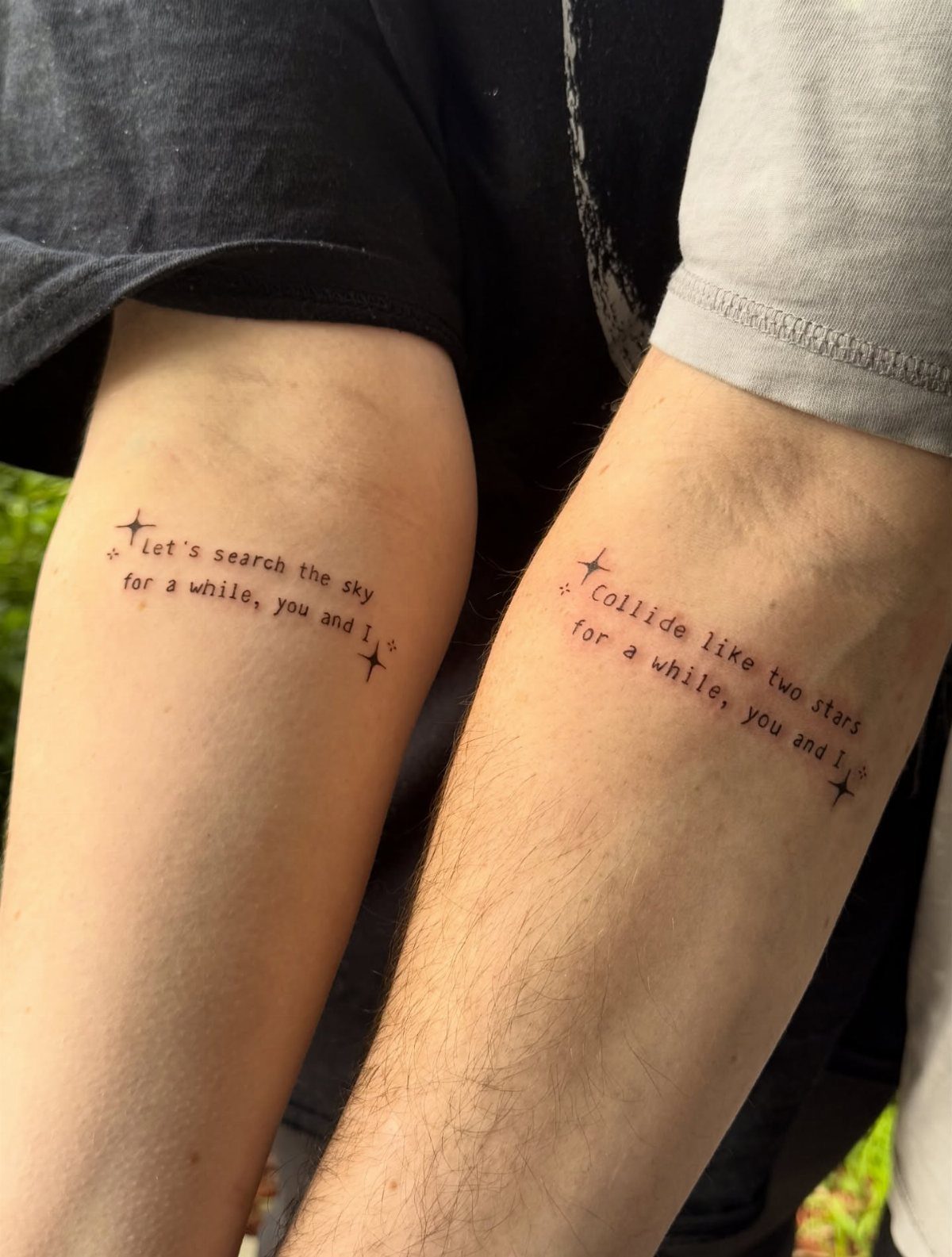 Two forearms with matching poetic text tattoos and small stars in black ink.
