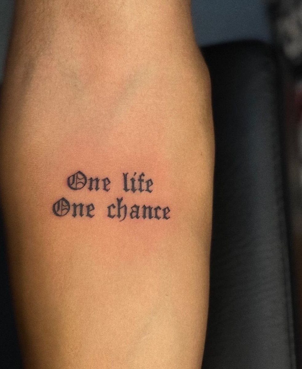 Forearm tattoo with gothic text reading One life One chance in black ink