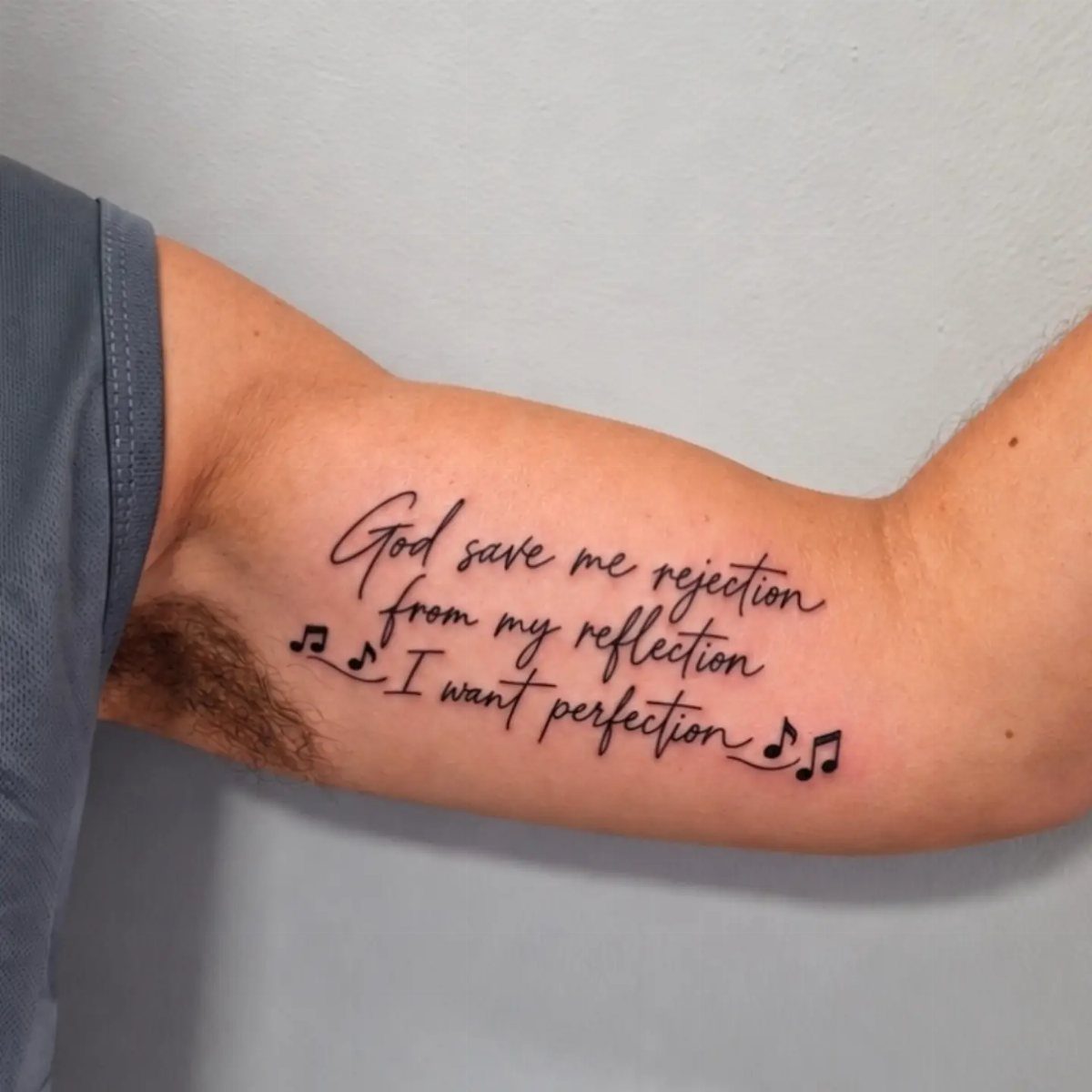 Cursive tattoo on a forearm with song lyrics and small musical notes.